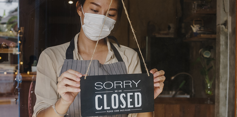 Young Asia girl wear face mask turning a sign from open to closed sign on glass door cafe after coronavirus lockdown quarantine. Owner small business, food and drink, business financial crisis concept