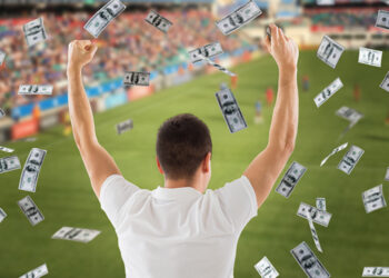 online betting, gambling and sport concept - happy man with raised hands and money rain over football field background
