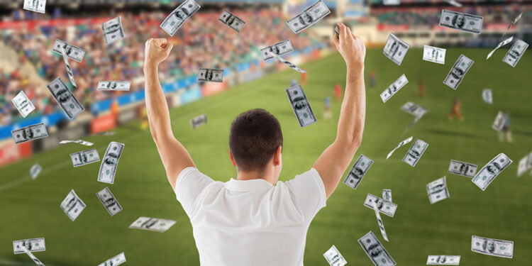 online betting, gambling and sport concept - happy man with raised hands and money rain over football field background