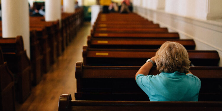 senior woman praying at a pew in church