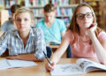 Serious girls sitting by desk and looking at blackboard at lesson