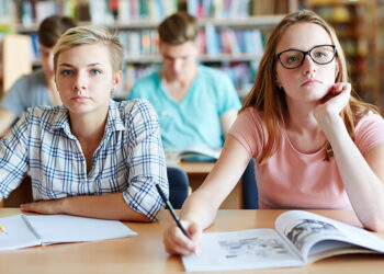 Serious girls sitting by desk and looking at blackboard at lesson