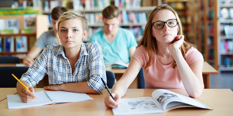 Serious girls sitting by desk and looking at blackboard at lesson